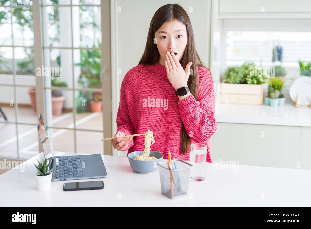Beautiful Asian woman working using laptop and eating asian noodles ...