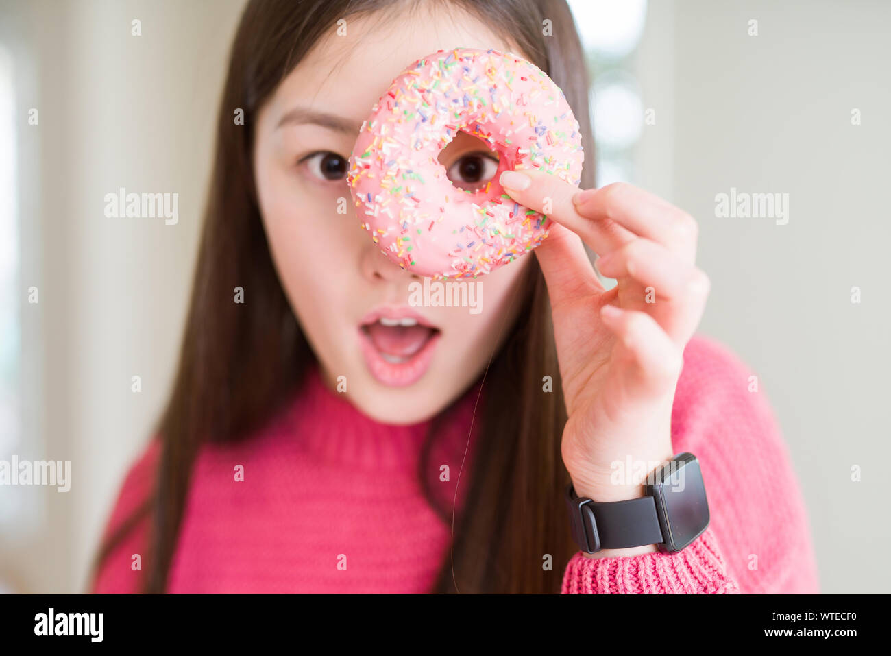 Beautiful Asian Woman Eating Pink Sugar Donut Scared In Shock With A Surprise Face Afraid And 