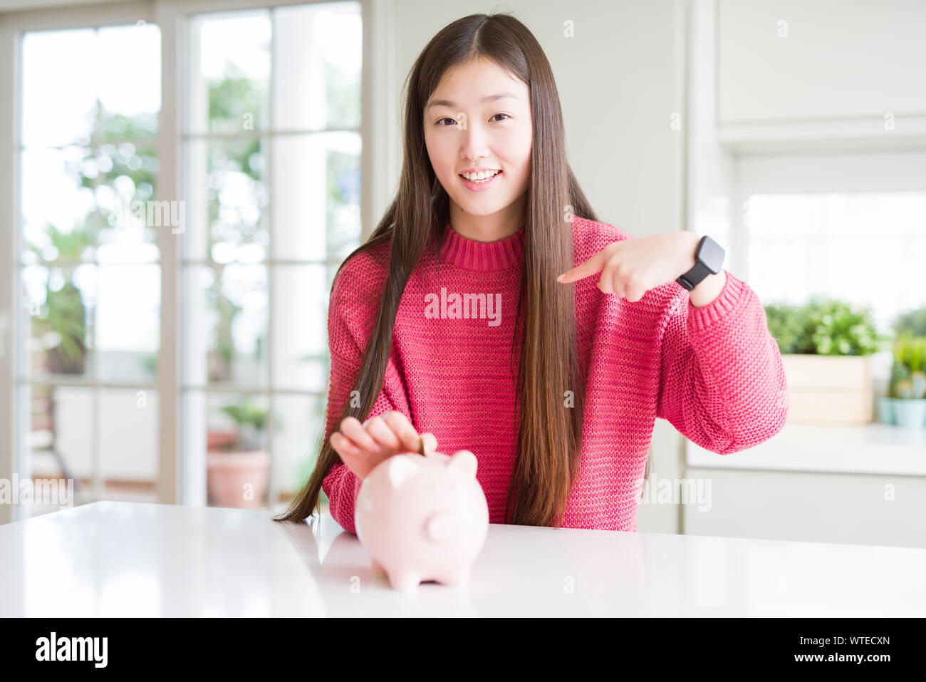 Beautiful Asian woman putting a coin inside piggy bag with surprise ...