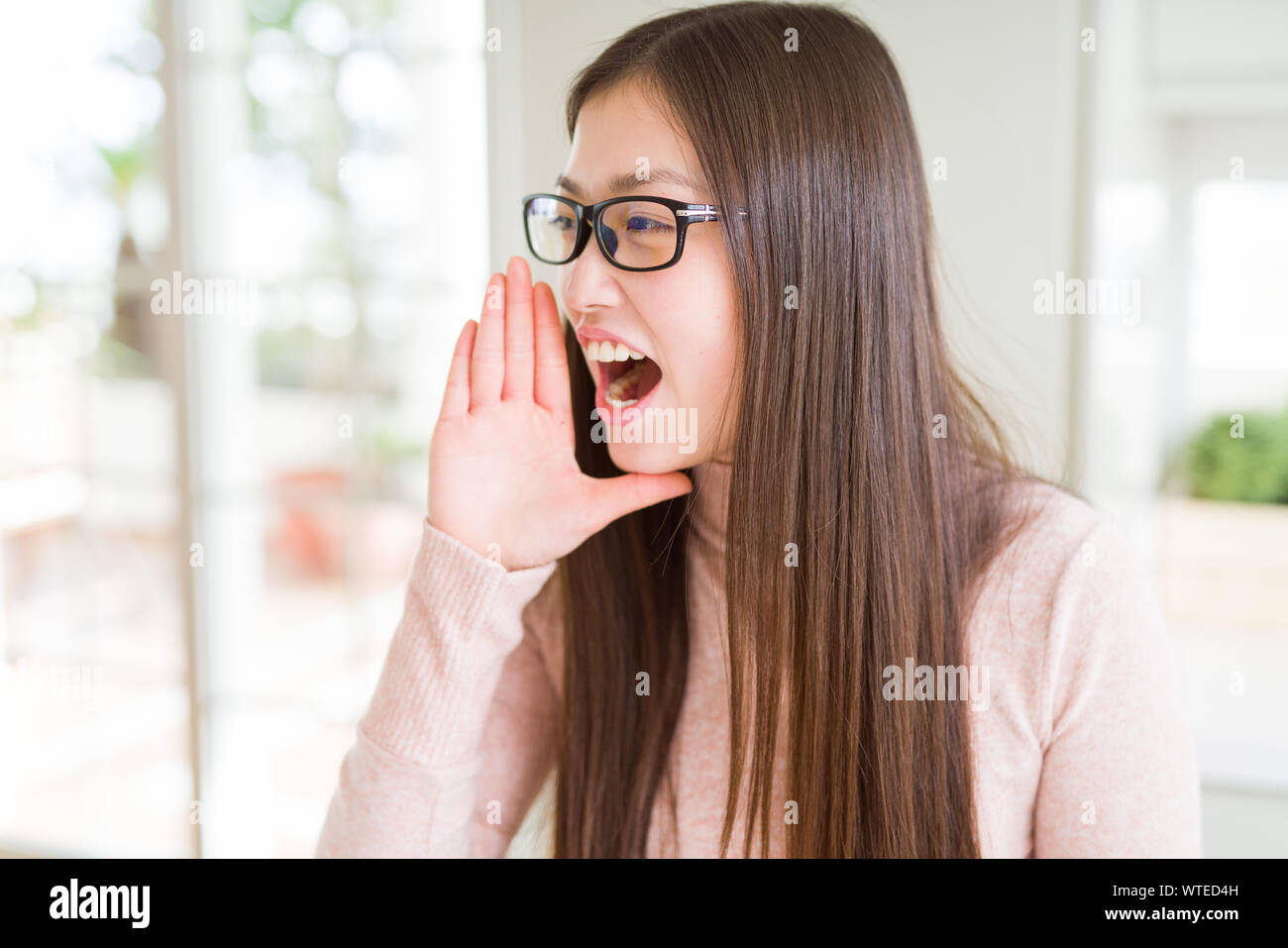 Beautiful Asian woman wearing glasses shouting and screaming loud to ...