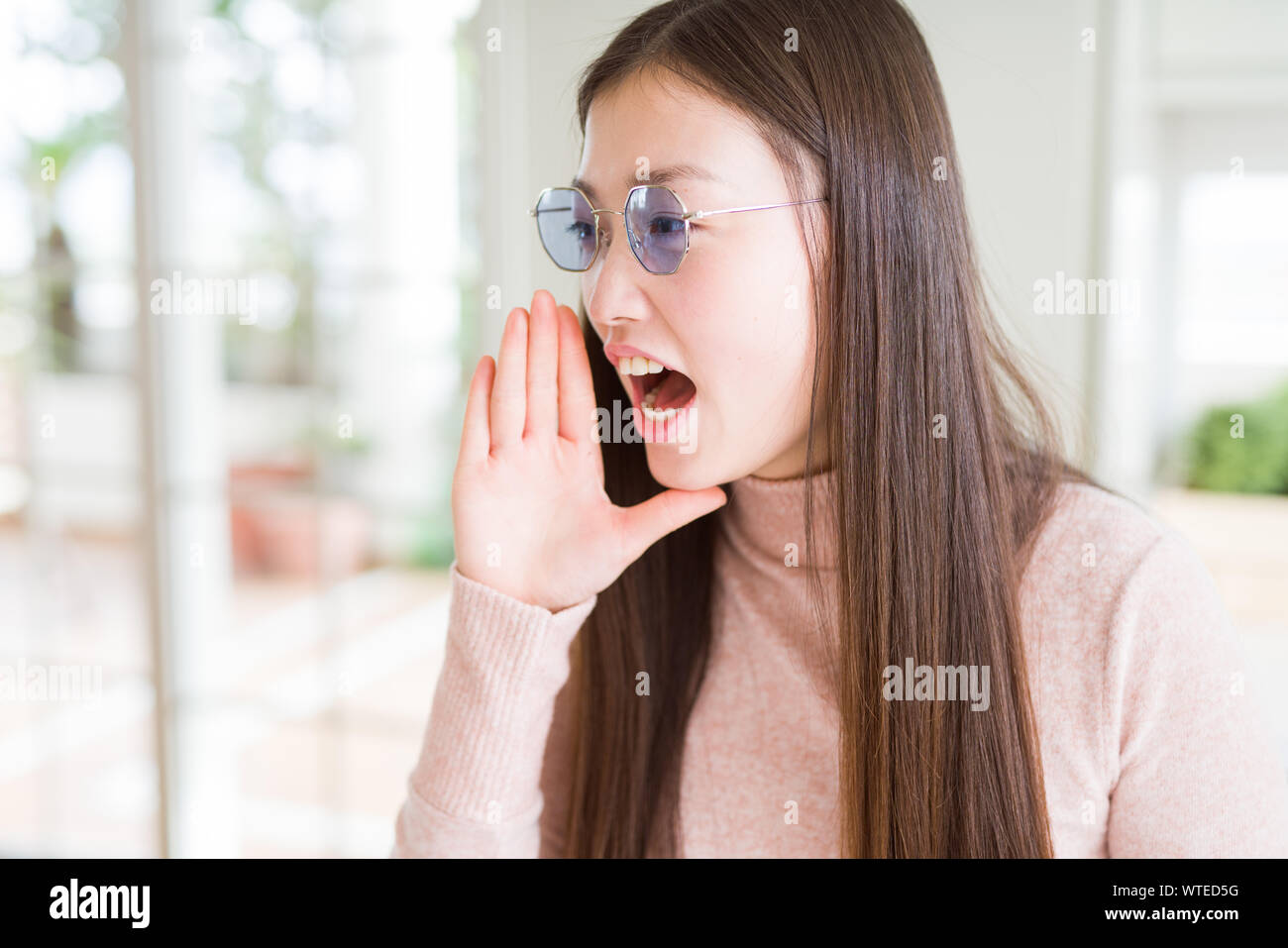 Beautiful Asian woman wearing glasses shouting and screaming loud to ...