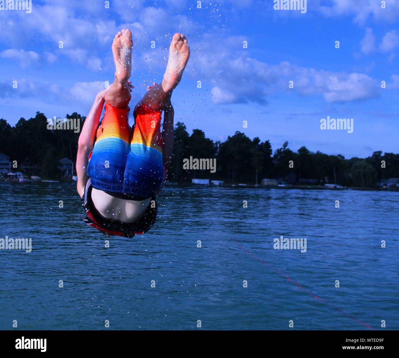 Man Wearing Multi Colored Swimming Trunks Diving In Sea Against Sky Stock Photo