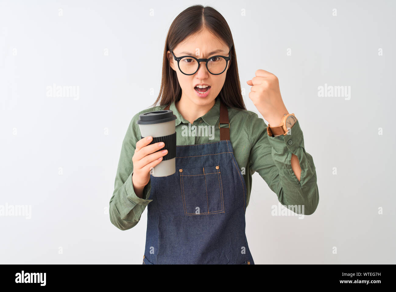 Chinese barista woman wearing apron glasses drinking coffee over isolated white background annoyed and frustrated shouting with anger, crazy and yelli Stock Photo