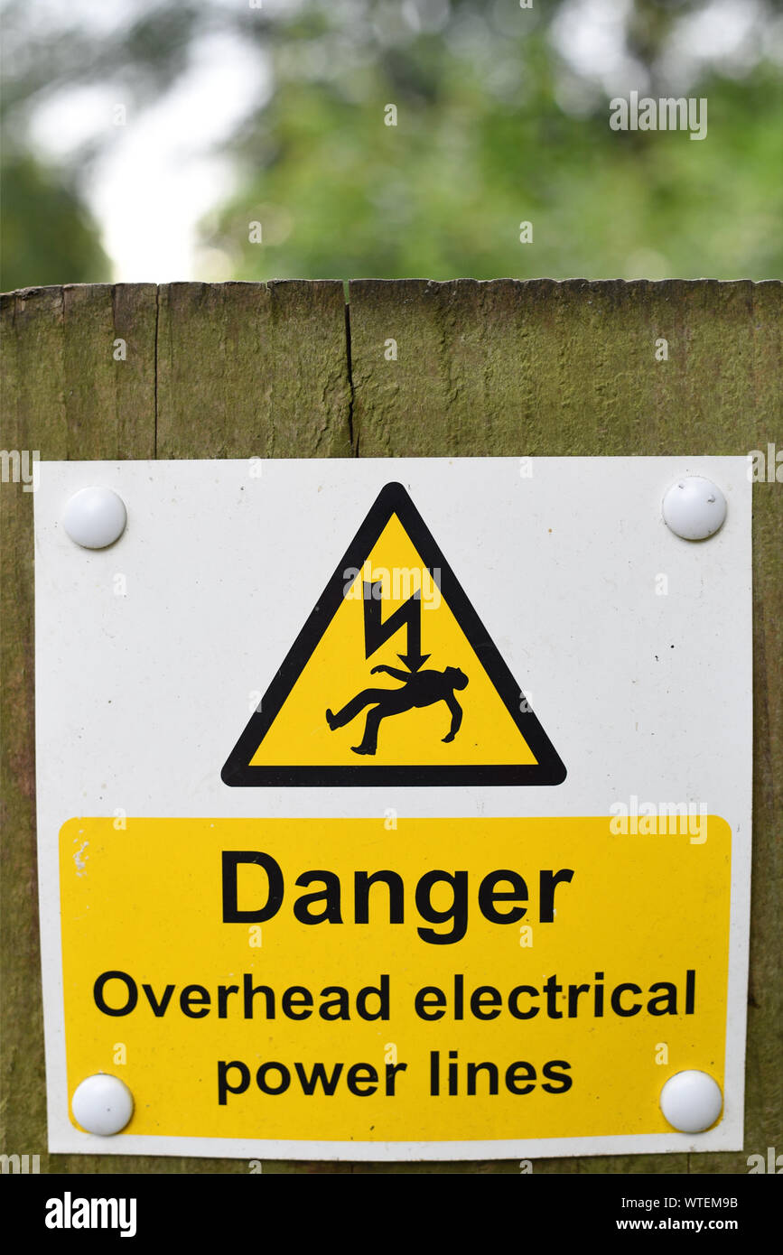 Danger overhead electrical power lines warning sign on wooden post with out of focus background Stock Photo