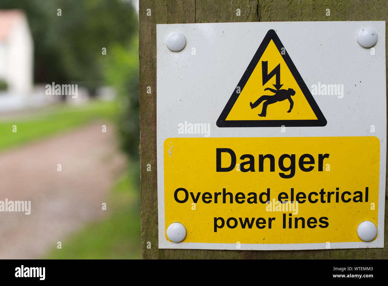Danger overhead electrical power lines warning sign on wooden post with out of focus background Stock Photo