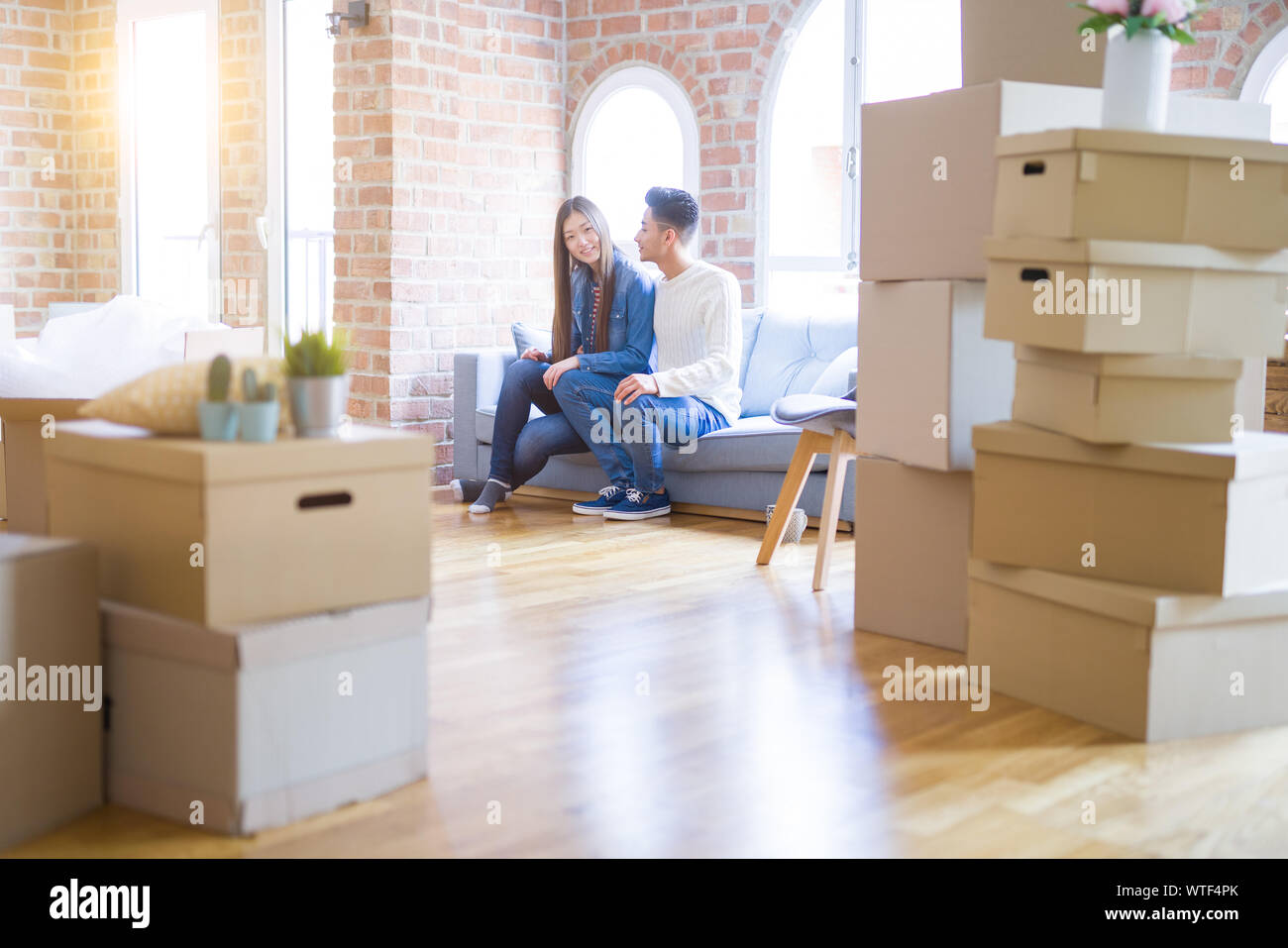 Beautiful young asian couple relaxing together sitting on the sofa arround cardboard boxes, happy moving to a new house Stock Photo