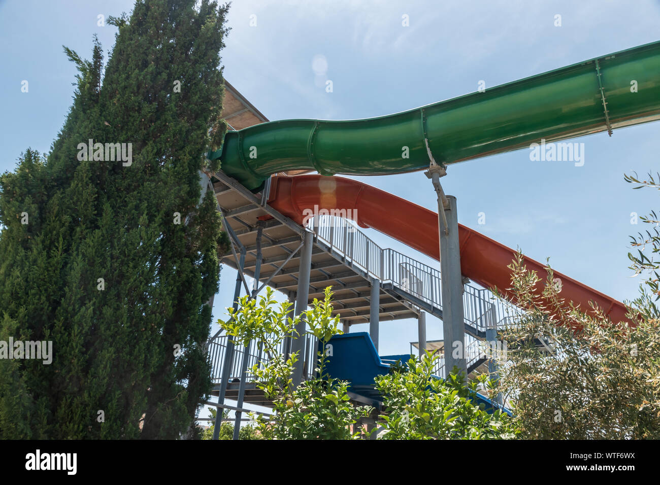 Here is the aqua park water slides. Green, red and blue water slided. Blue sky with green trees. Stock Photo