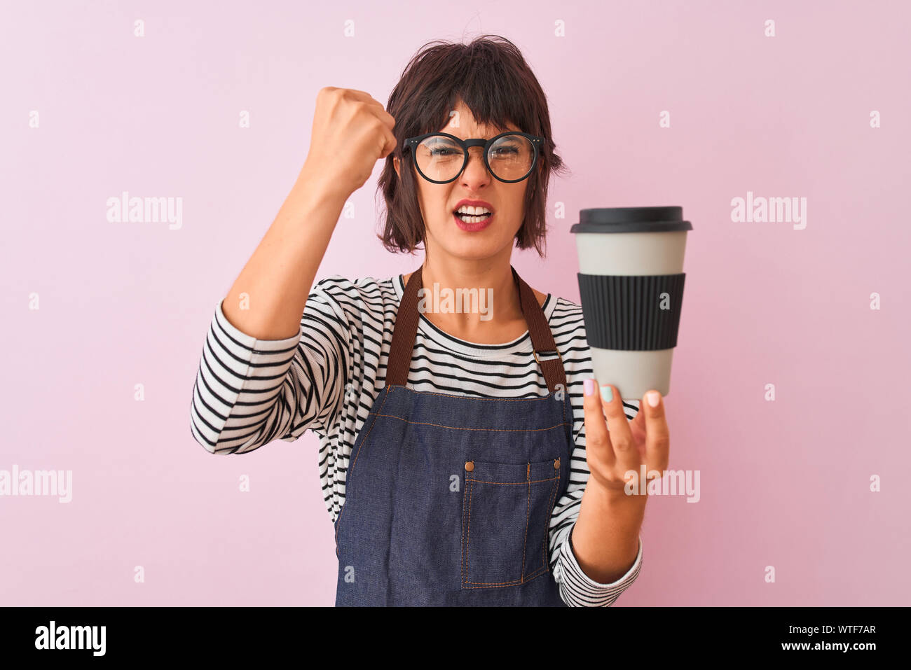 Young beautiful barista woman wearing glasses holding coffee over isolated pink background annoyed and frustrated shouting with anger, crazy and yelli Stock Photo