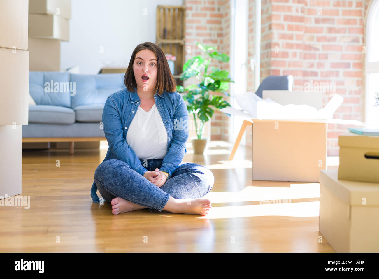 Young plus size woman sitting on the floor around cardboard boxes