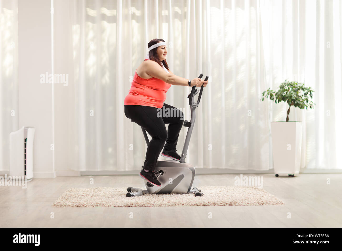 Overweight woman exercising on a stationary bike at home Stock Photo