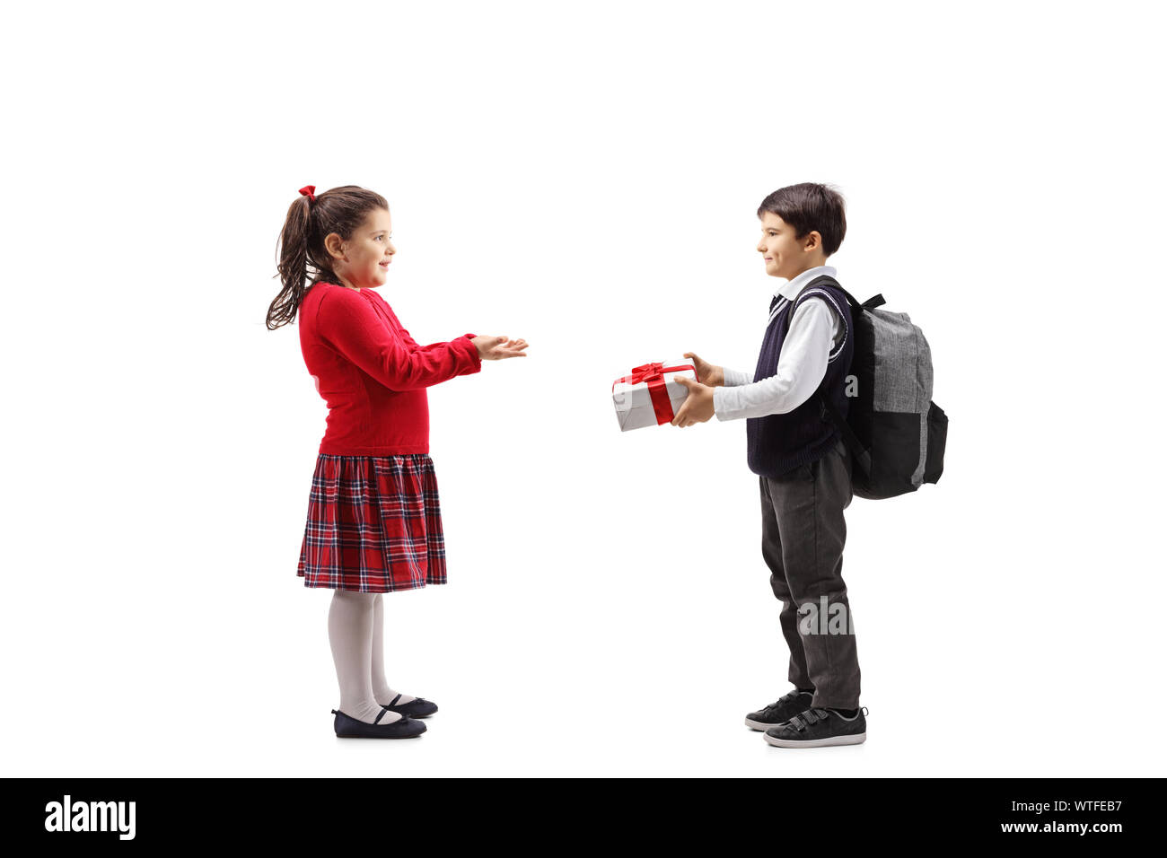 Full length profile shot of a schoolboy giving a gift box to a girl in a red dress isolated on white background Stock Photo