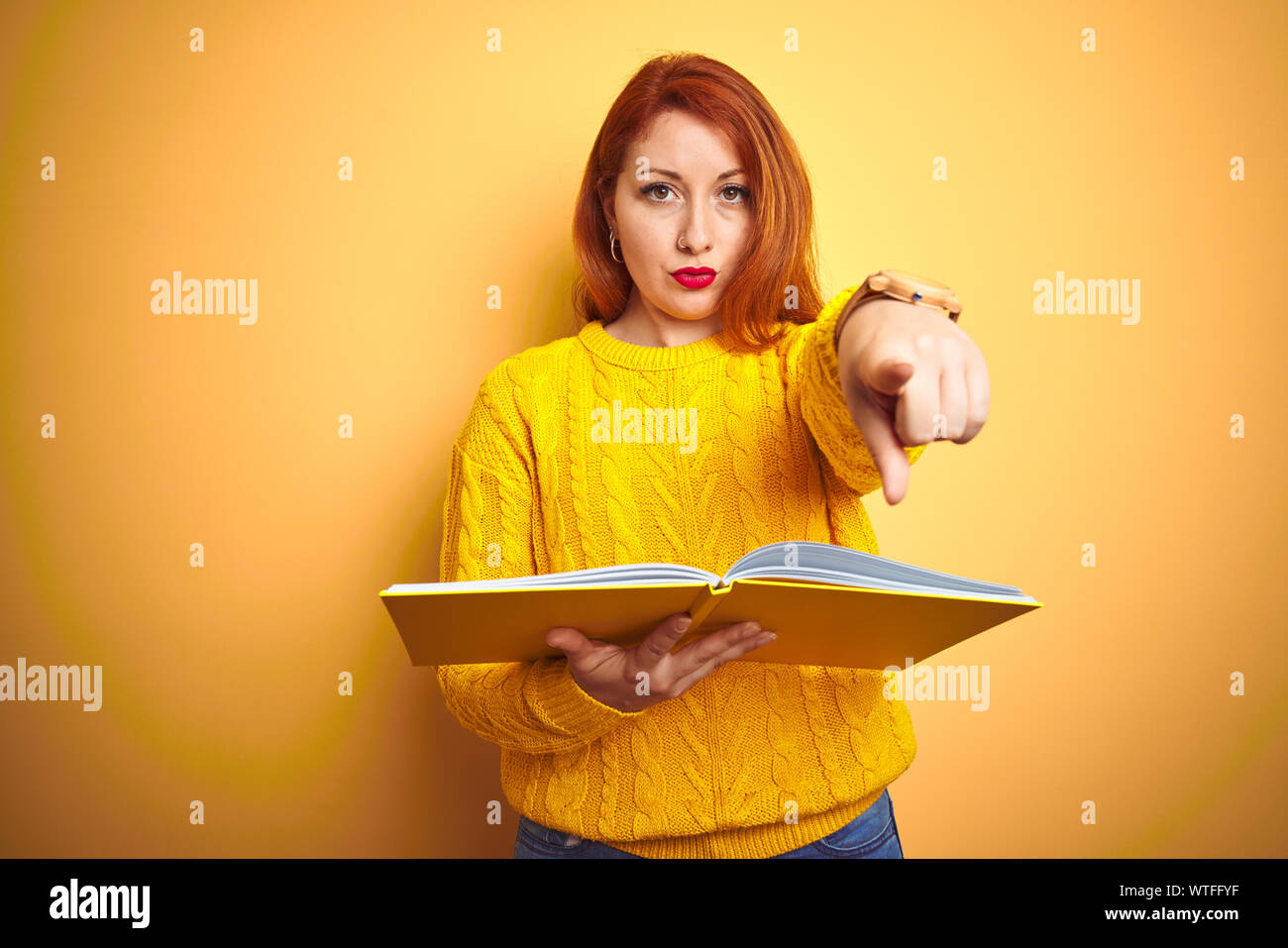 Young redhead student woman reading book standing over yellow isolated ...