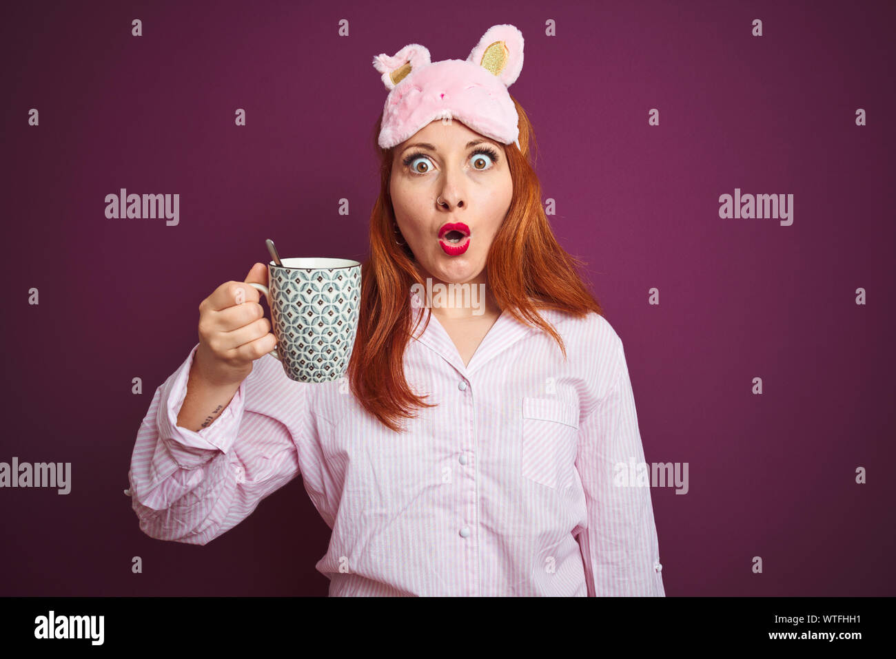Young redhead woman wearing pajama drinking coffee over purple isolated background scared in