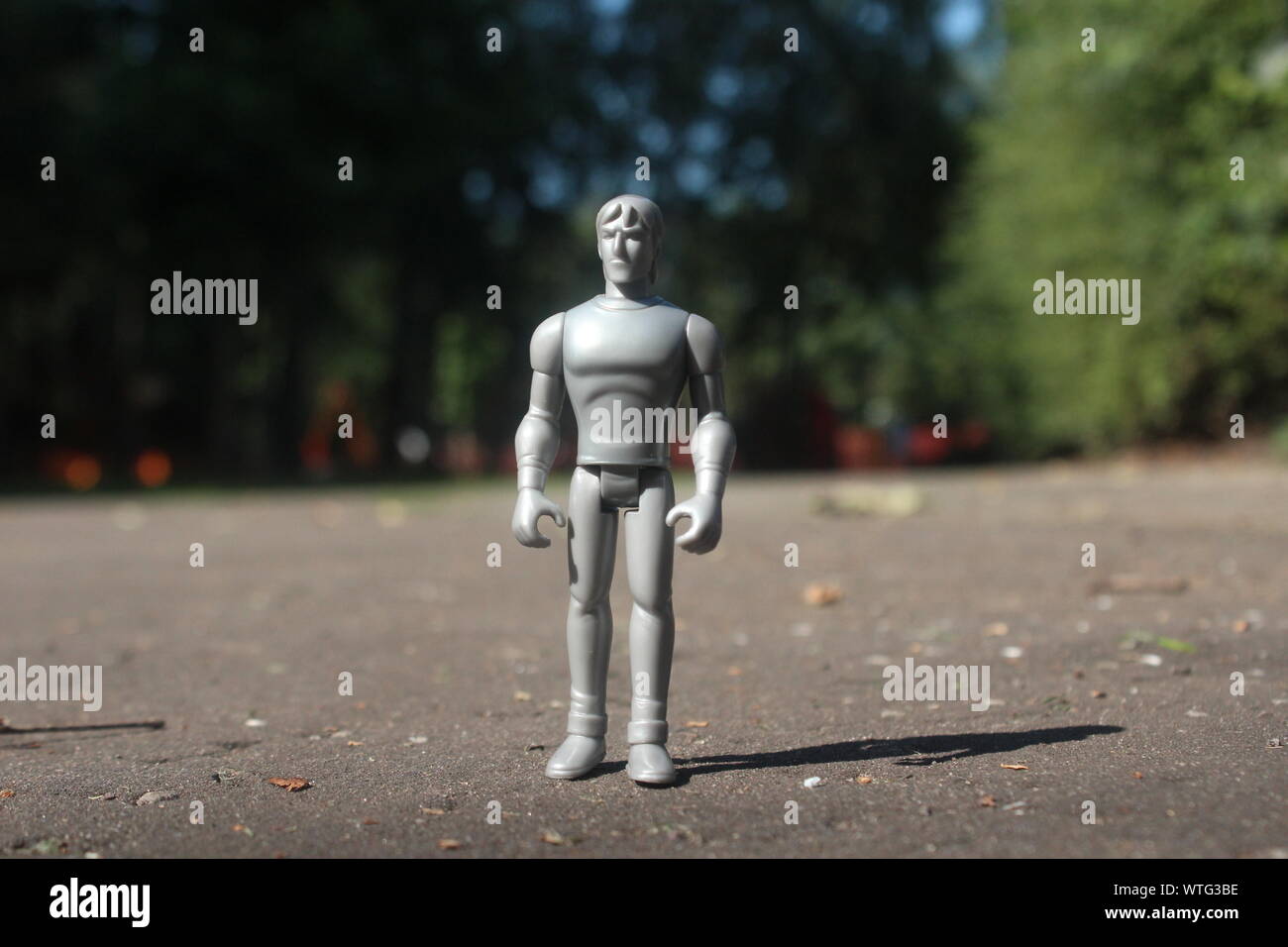 Close up small grey action figure brought to life standing on a park pathway on a bright day Stock Photo