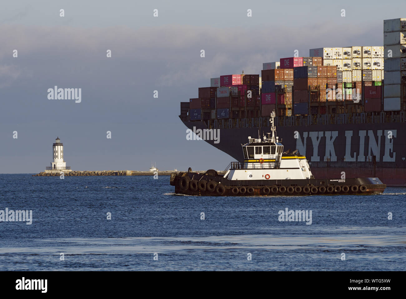 Image showing an NYK Line container ship departing from the Port of Los Angeles as well as a tugboat and the Angeles Harbor Light. Stock Photo