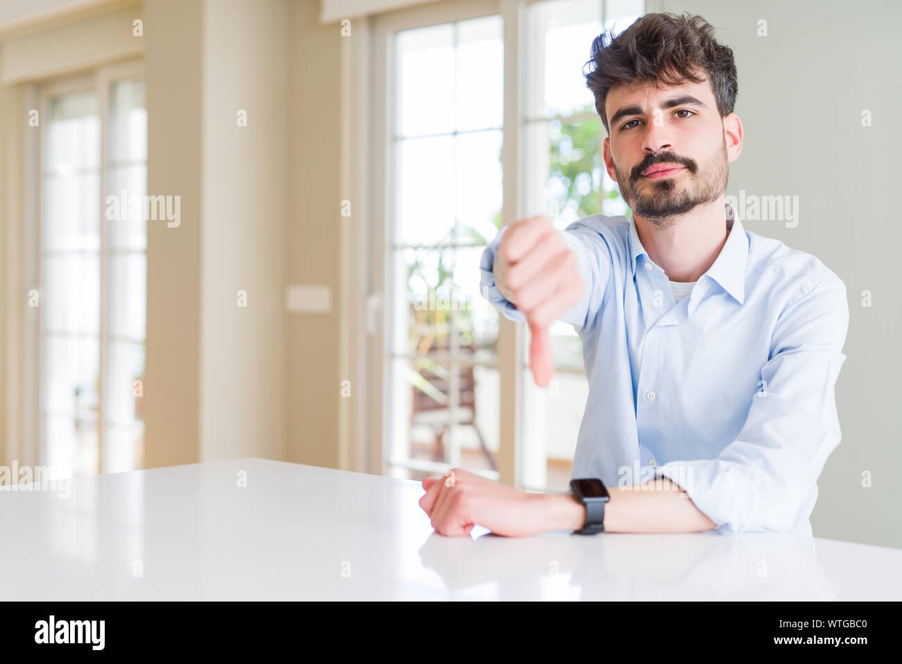 Young businesss man sitting on white table looking unhappy and angry ...