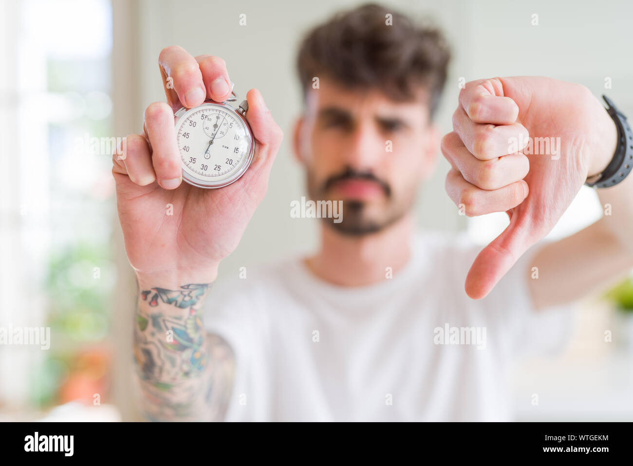 Young man using holding stopwatch with angry face, negative sign ...