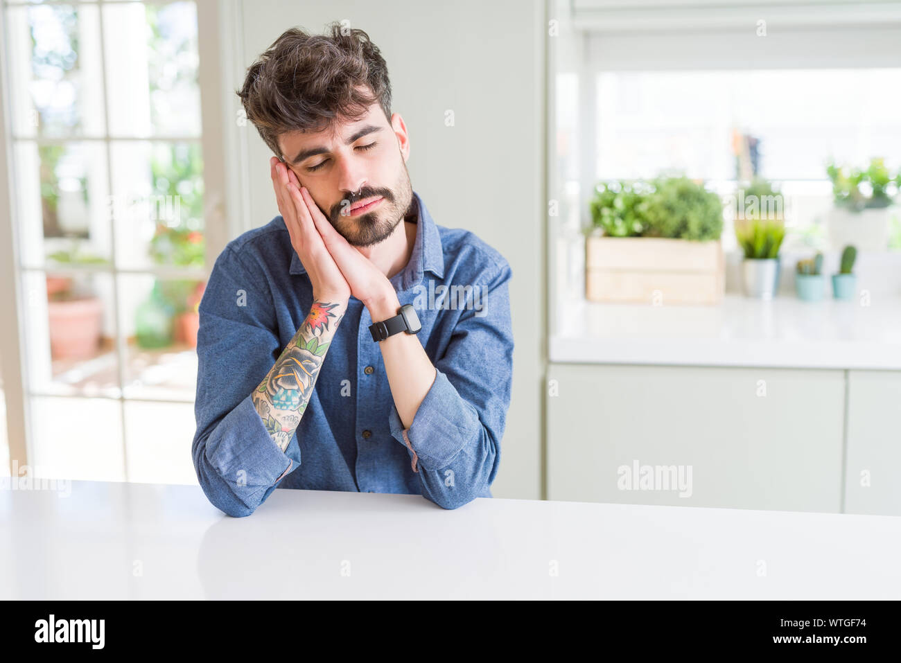 Young man wearing casual shirt sitting on white table sleeping tired ...