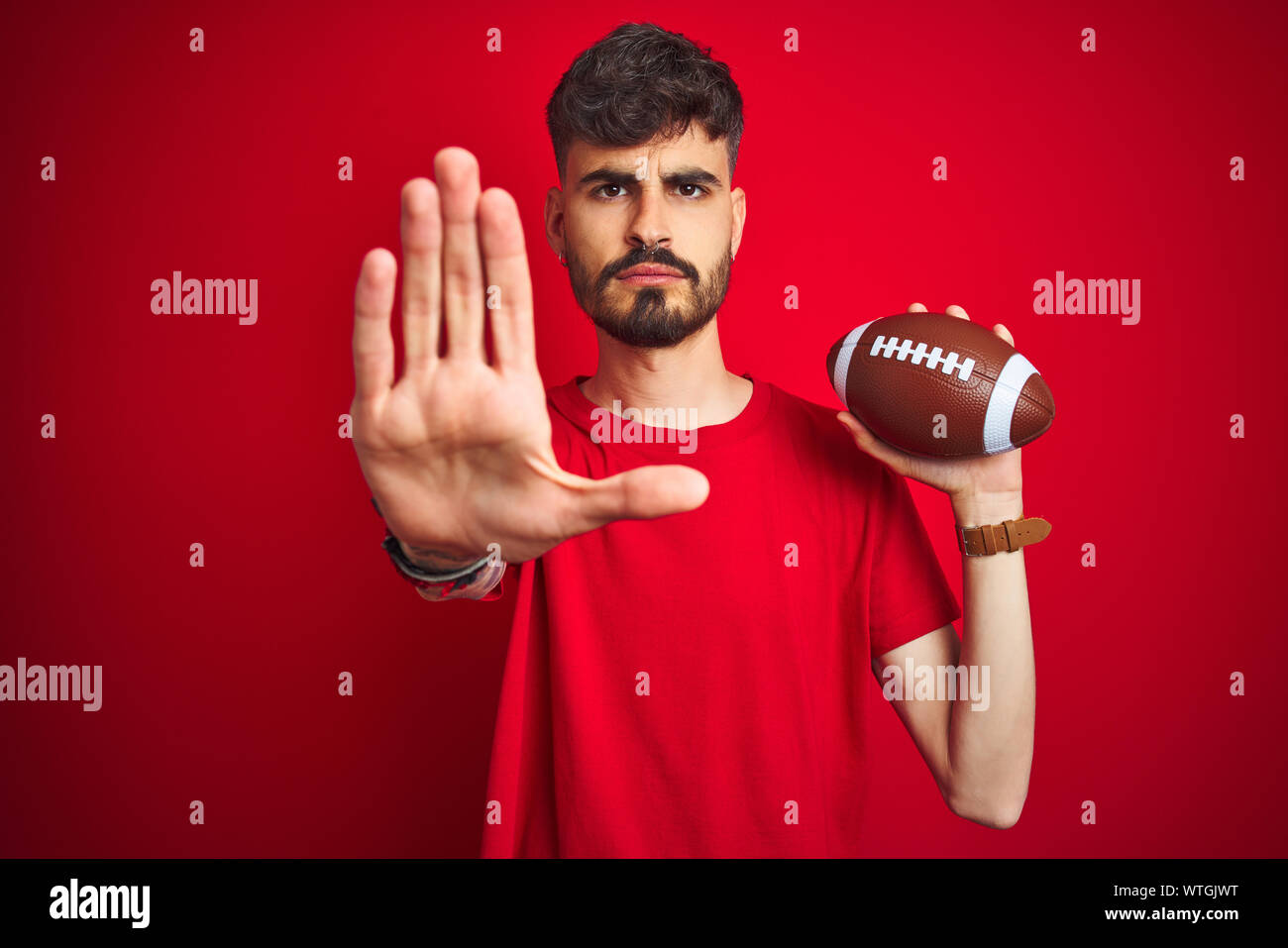 Young athlete man with tattoo holding football ball standing over ...