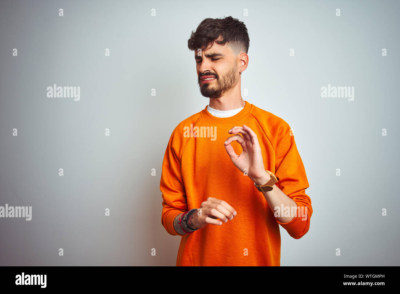 Young man with tattoo wearing orange sweater standing over isolated white background disgusted expression, displeased and fearful doing disgust face b Stock Photo