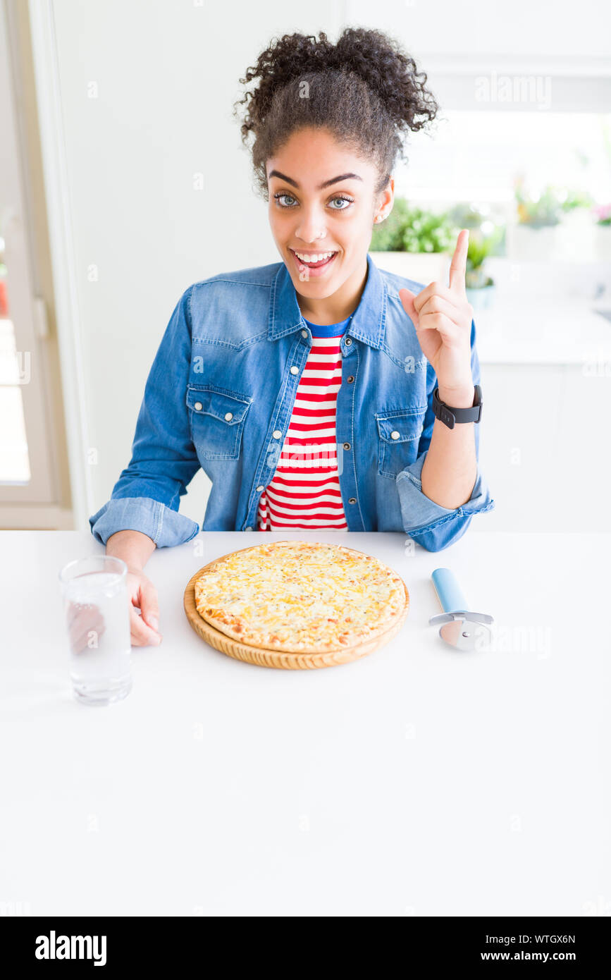 Young african american woman eating homemade cheese pizza surprised with an idea or question