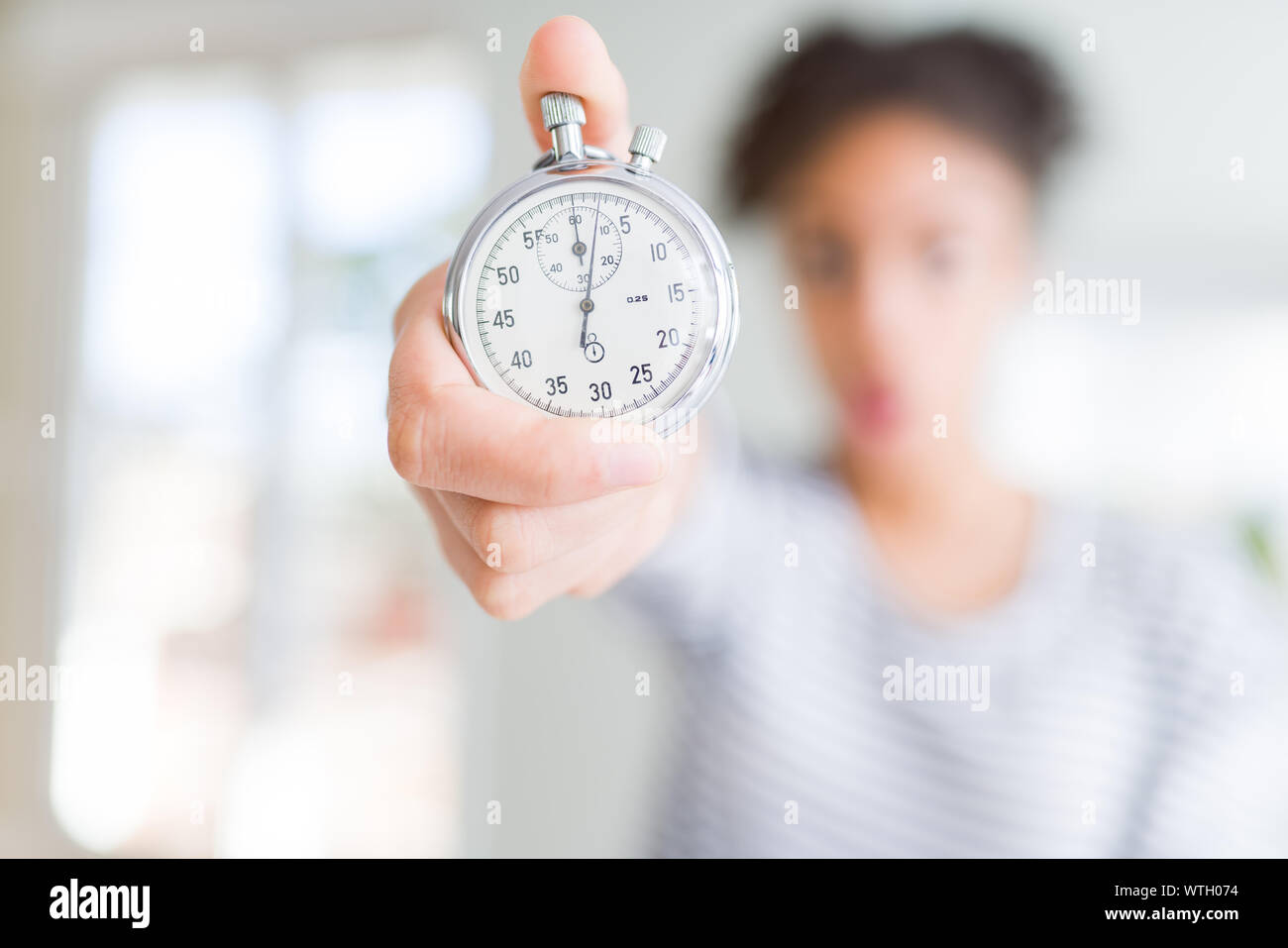 Young african american woman holding stopwatch scared in shock with a ...