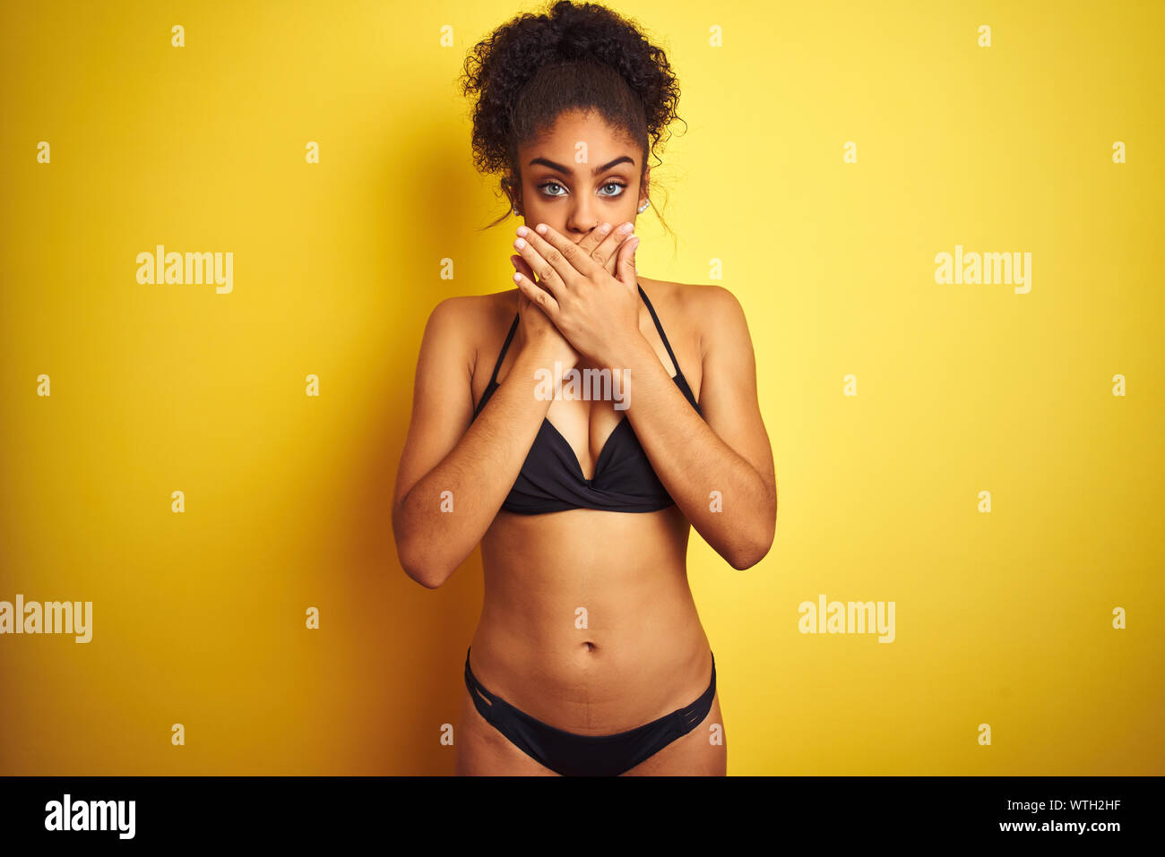 African american woman on vacation wearing bikini standing over isolated  yellow background shocked covering mouth with hands for mistake. Secret  conce Stock Photo - Alamy