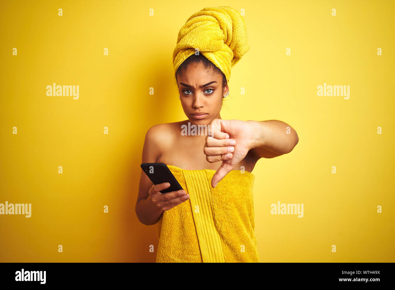 Afro woman wearing towel after shower using smatrphone over isolated