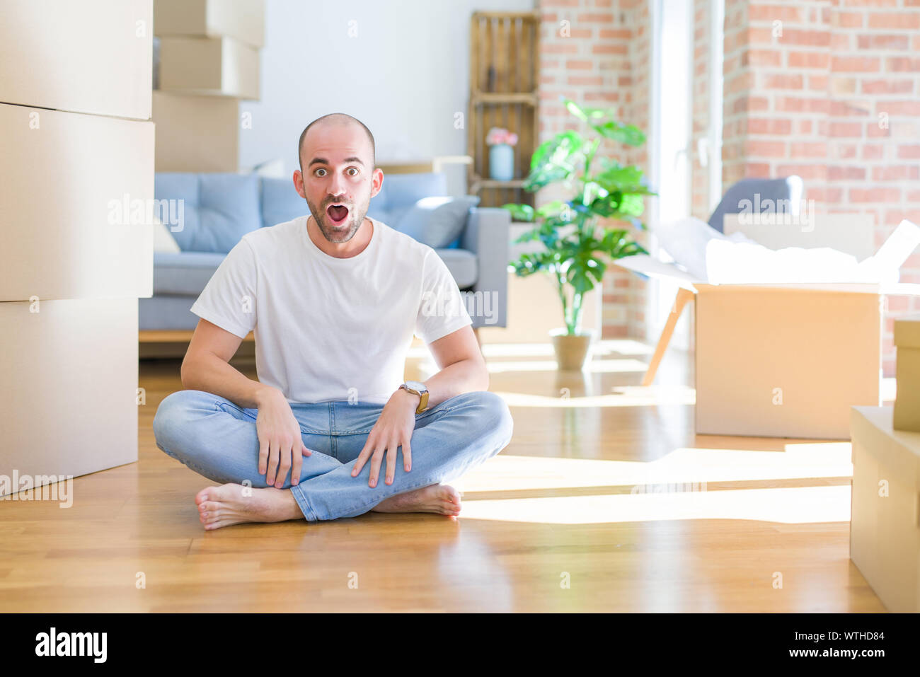 Young bald man sitting on the floor around cardboard boxes moving to a