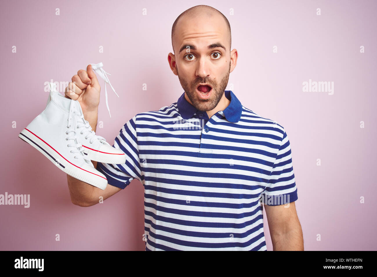 Young man holding casual sneakers shoes over pink isolated background
