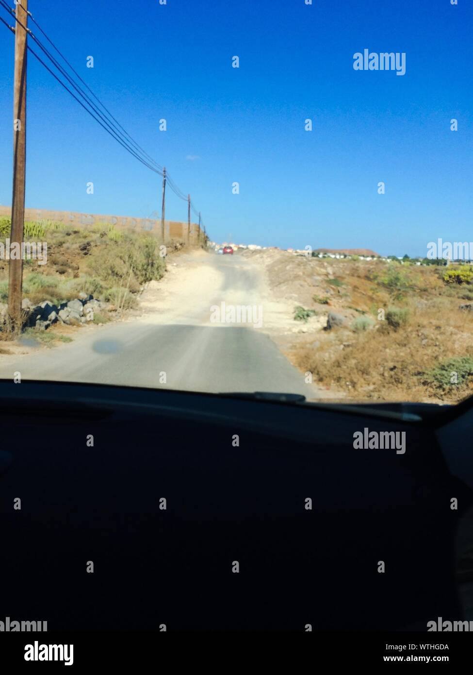 Cropped Image Of Car On Single Lane Road Against Clear Blue Sky Stock Photo