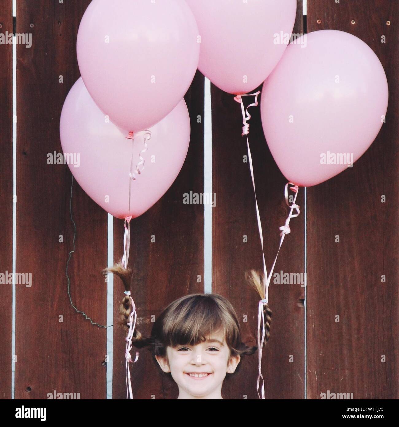 Portrait Of Happy Girl With Pink Helium Balloons Tied On Ponytails Stock Photo