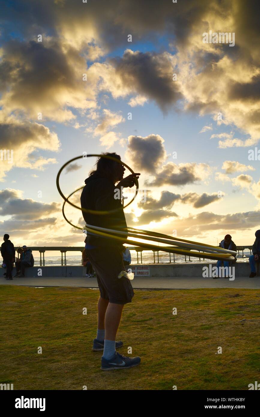 Man practicing spinning rings hoops in park, with bohemian, hippie crowd relaxing during sunset, Ocean Beach (OB) in San Diego, California, USA Stock Photo