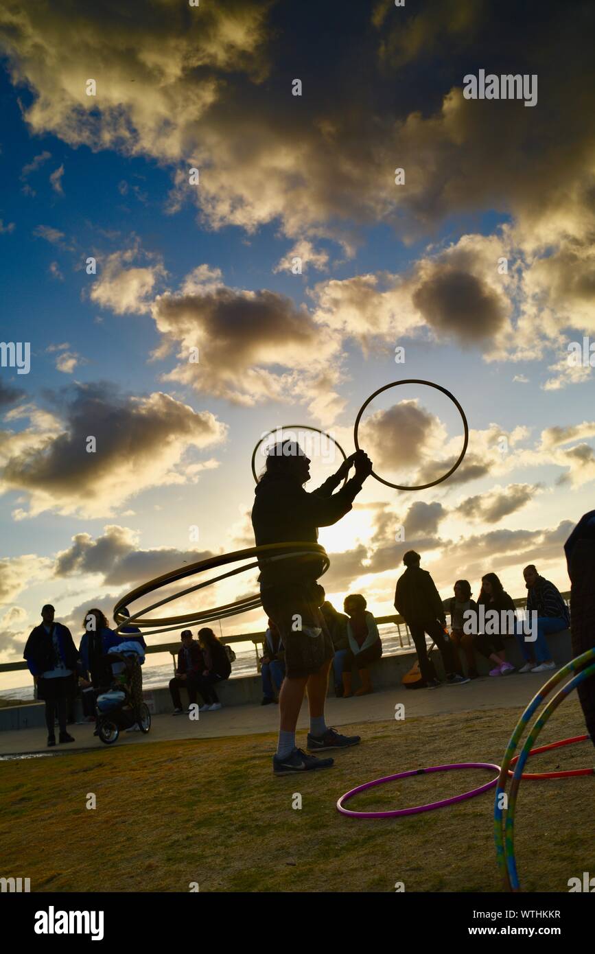 Man practicing spinning rings hoops in park, with bohemian, hippie crowd relaxing during sunset, Ocean Beach (OB) in San Diego, California, USA Stock Photo