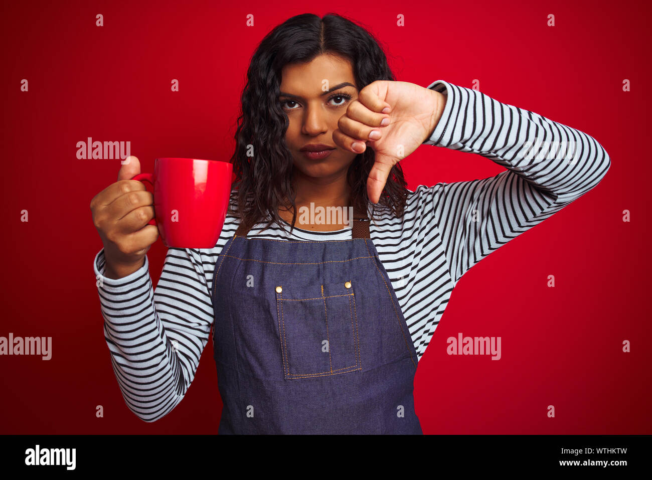 Transsexual transgender barista woman holding cup of coffee over isolated red background with angry face, negative sign showing dislike with thumbs do Stock Photo
