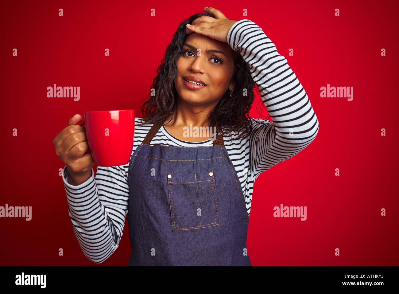 Transsexual transgender barista woman holding cup of coffee over isolated red background stressed with hand on head, shocked with shame and surprise f Stock Photo