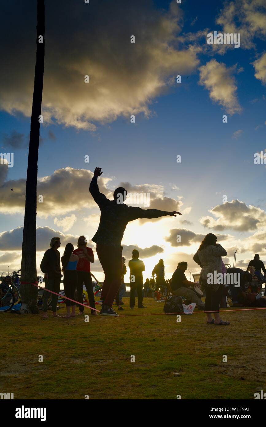 Tight rope practice in park, with bohemian, hippie, unconventional artsy crowd relaxing during sunset, Ocean Beach (OB) in San Diego, California, USA Stock Photo