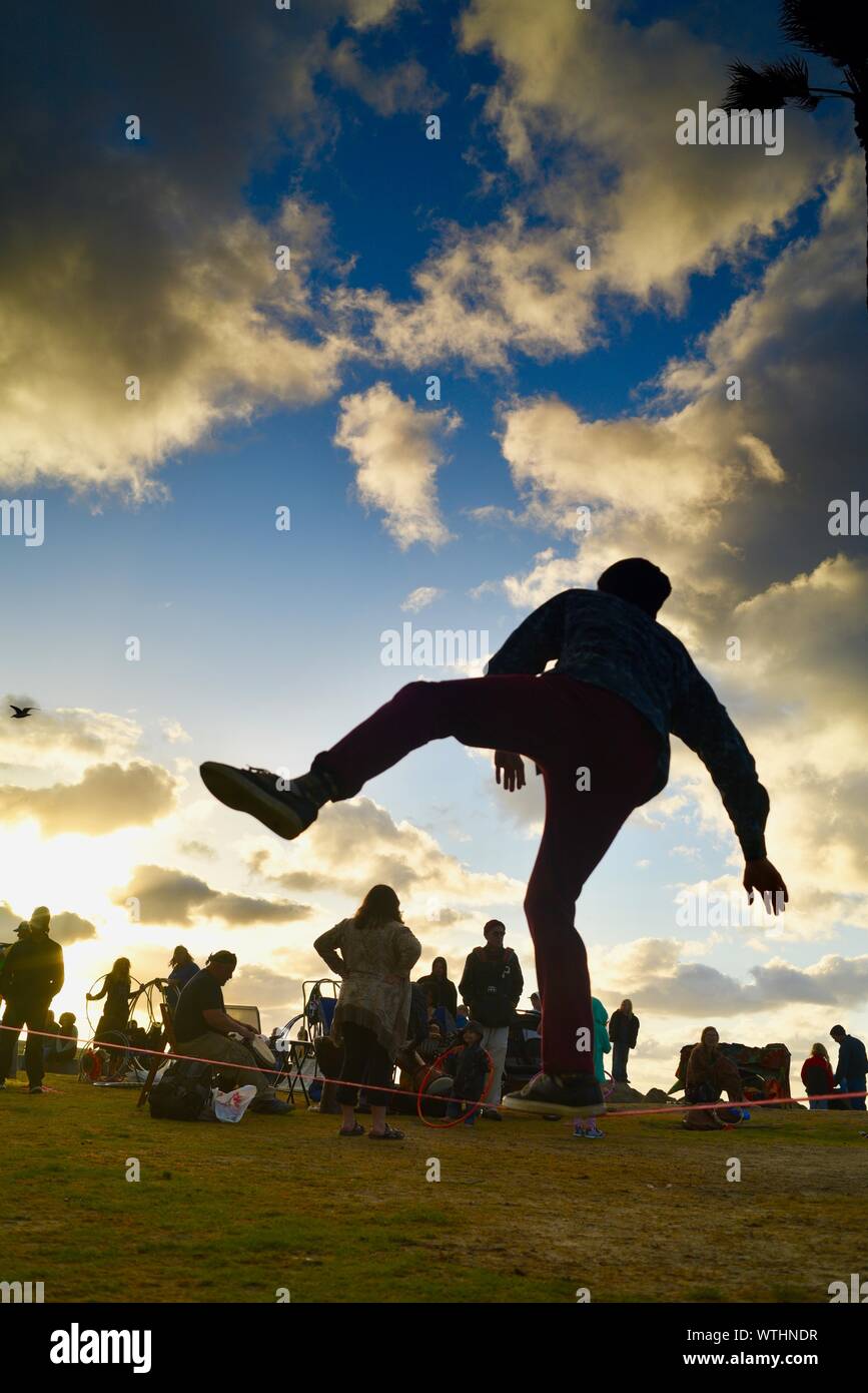 Tight rope practice in park, with bohemian, hippie, unconventional artsy crowd relaxing during sunset, Ocean Beach (OB) in San Diego, California, USA Stock Photo