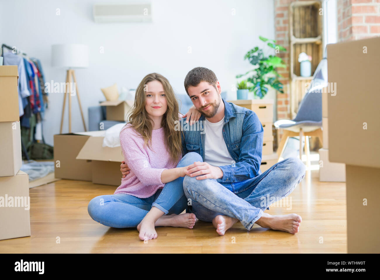 Young beautiful couple moving to a new house sitting on the floor with ...
