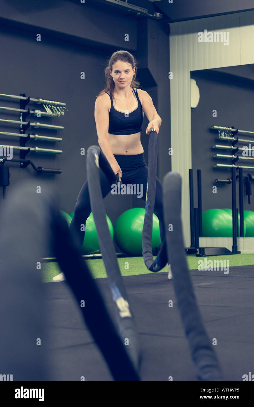 Young athletic woman exercising in gym using battle rope. Stock Photo