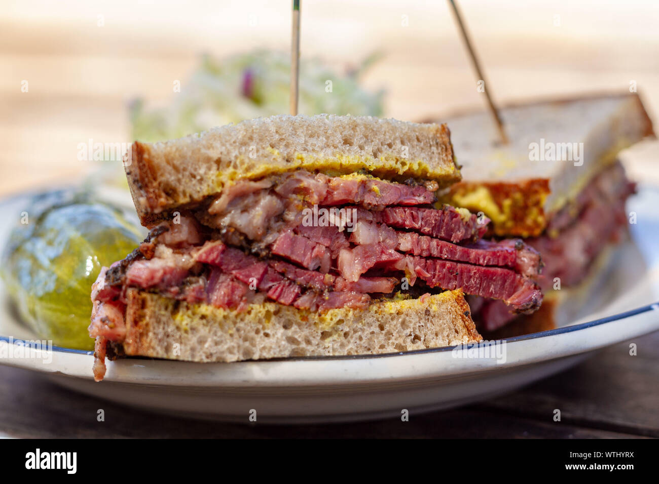 Pastrami sandwich sliced in half on rye bread with mustard on a white