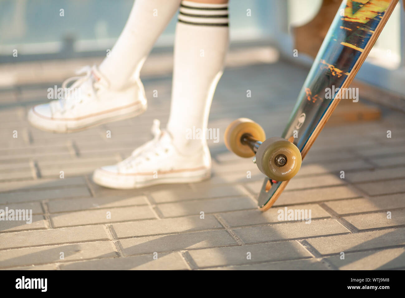 Stylish young girl sitting on bus stop with her longboard, drink soda
