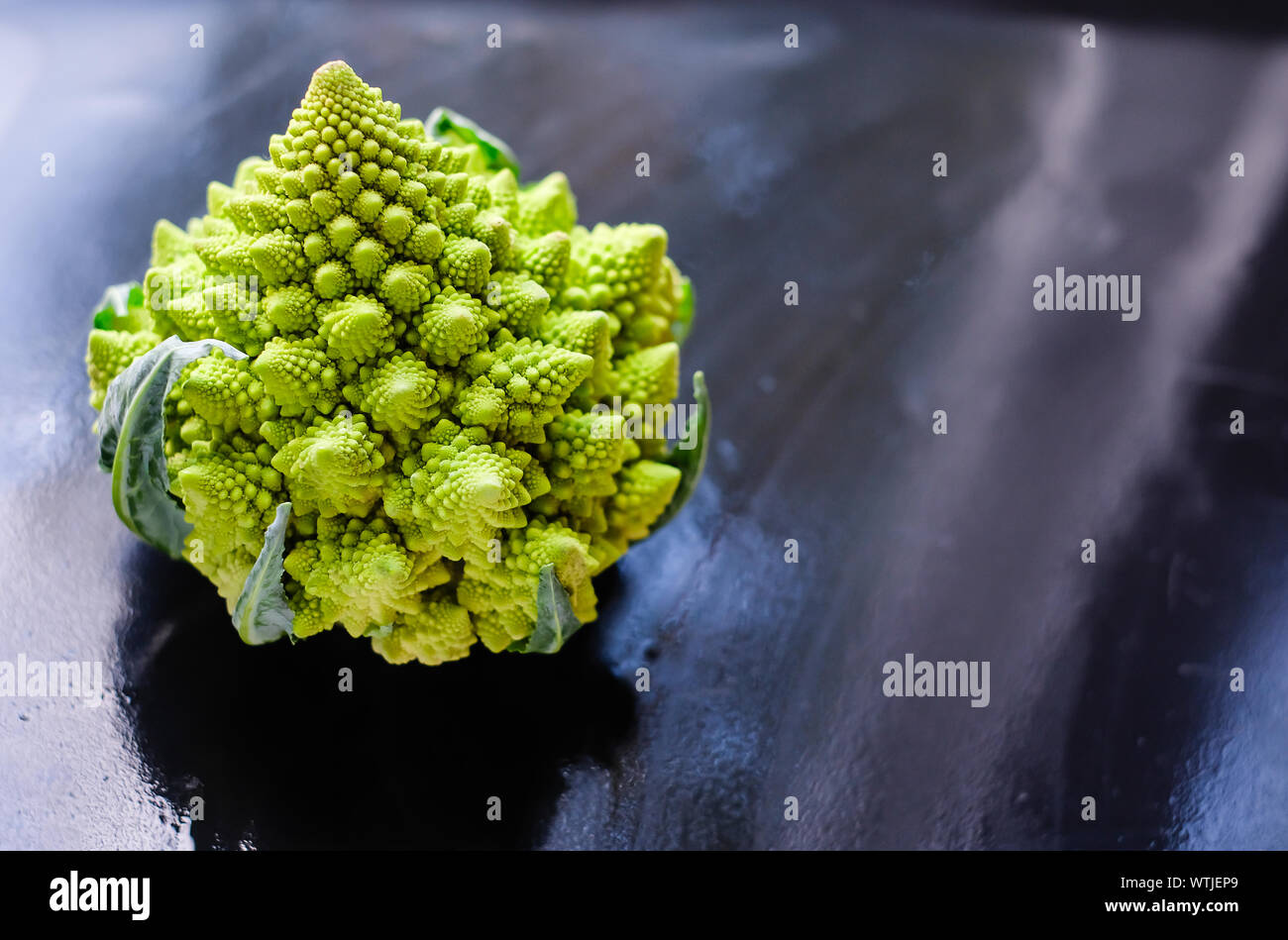 Amazing fresh green Romanesco broccoli or Roman cauliflower on wet dark background. Its form is a natural approximation of a fractal. Close up view. Stock Photo