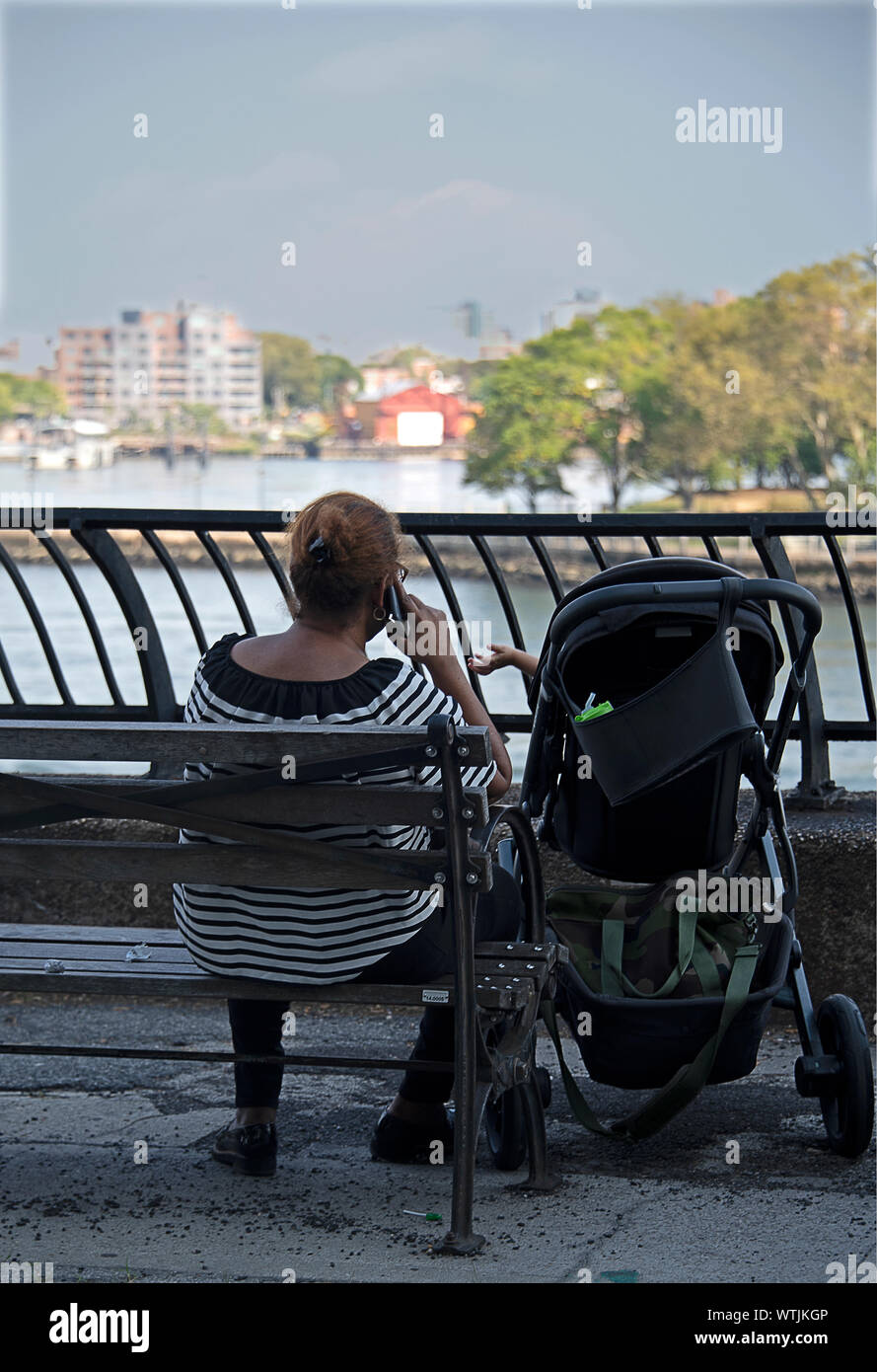 Baby reaching out to caregiver, she is on her phone and too busy to notice. Stock Photo