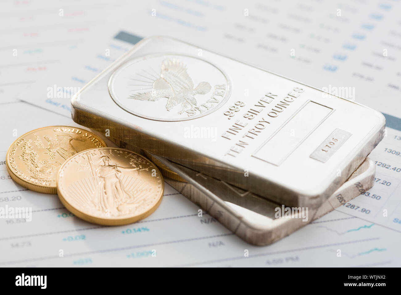 Gold ingots and Gold Eagle coins on stock market data Stock Photo