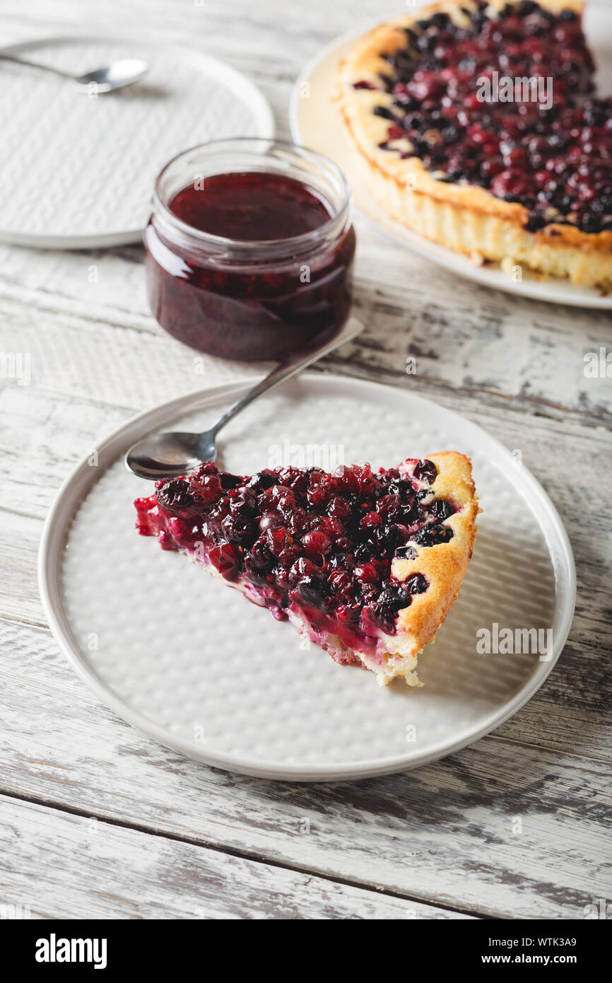 Piece of berry pie with cherry, currant, blackberry, blueberry with kitchenware and recipe mockup on white wooden table . Cheesecake, top view with Stock Photo
