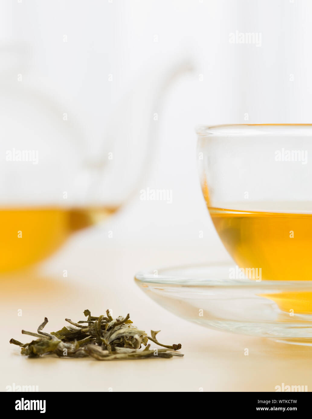 Cup of green tea and green tea leaves with teapot in background Stock Photo