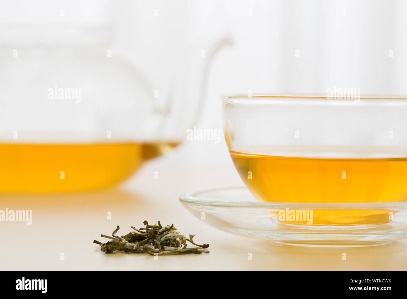 Cup of green tea and green tea leaves with teapot in background Stock Photo