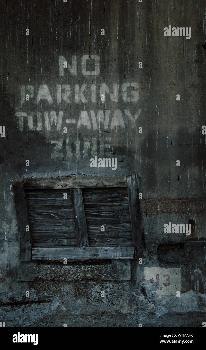 A dark, grungy image showing an old wooden pallet standing on its end under the words 'No Parking Tow-Away Zone' Stock Photo