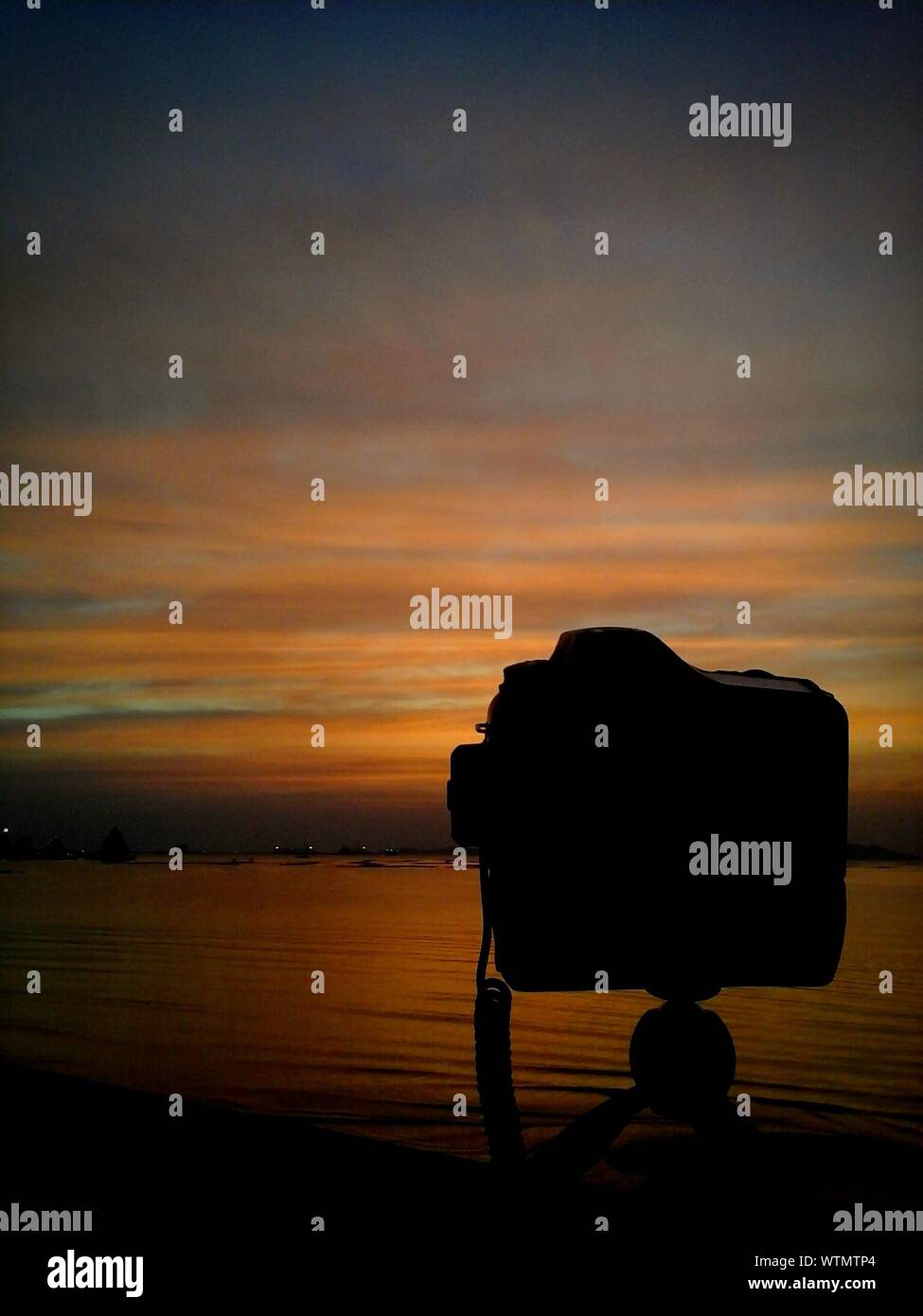 Scenic View Of Camera Silouhette By The Sea At Sunset Stock Photo